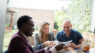 Three people sitting at a table and smiling while looking at documents